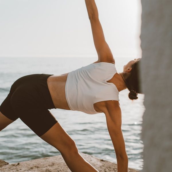 Person practicing a gentle stretching yoga pose outdoors at sunrise.